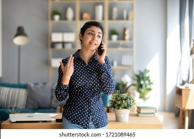 Happy millennial hindu student girl chatting on cellphone with friends. Smiling young indian businesswoman holding mobile phone call with clients, ordering taxi food, leaning on table at home.