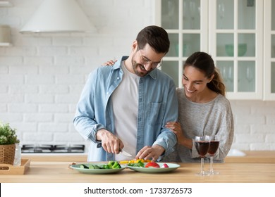 Happy Millennial Husband And Wife Stand At Counter Cooking Dinner Salad Together, Smiling Young Caucasian Couple Have Fun Preparing Food In Home Kitchen Enjoy Family Weekend Or Celebration