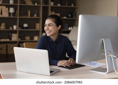 Happy millennial Indian employee satisfied with job, working at laptop, workstation monitor, typing, looking away, laughing. Young business woman, professional, marketing finance analyst at workplace - Shutterstock ID 2086007983