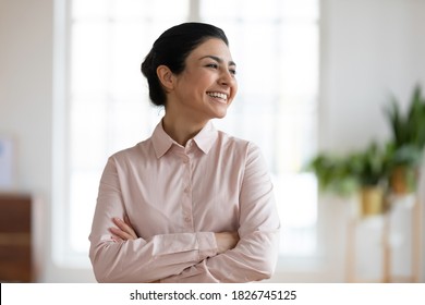 Happy millennial indian female employee look in window distance feel optimistic motivated about future career success. Smiling young ethnic woman think dream of opportunities. Business vision concept.