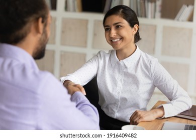 Happy Millennial Indian Female Employee Shake Hand Get Acquainted With African American Man Client Or Customer. Smiling Diverse Multiracial Businesspeople Handshake Close Deal At Office Meeting.