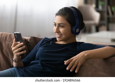 Happy millennial Indian woman in headphones have webcam digital virtual conference on cellphone. Smiling young ethnic female in earphones talk speak on video call on smartphone. Technology concept.