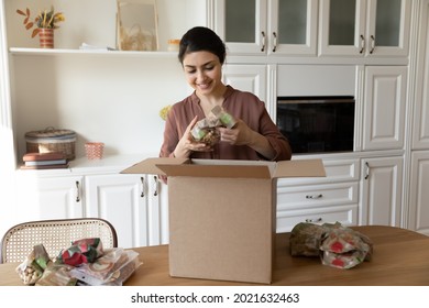 Happy millennial Indian woman open unbox package shopping online for healthy organic food. Smiling young ethnic female unpack box buy products on internet from home. Good delivery concept.