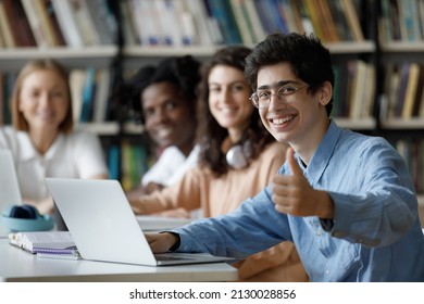 Happy millennial Jewish male student in eyeglasses showing thumbs up gesture, using computer, working on online project or preparing for exams in college library with smiling multiracial friends. - Shutterstock ID 2130028856