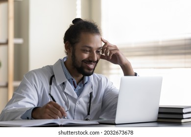 Happy millennial male african american multiracial gp doctor therapist physician watching medical educational healthcare video webinar on computer or reading pleasant news, working in hospital office.