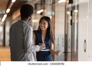 Happy Millennial Multiethnic Employees Stand In Modern Office Hallway Talking, Smiling Young Diverse Ethnic Colleagues Laugh Have Fun Speaking In Corridor, Company Multiethnic Interns Chatting