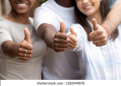 Happy millennial multi-ethnic girls guys standing close to each other showing thumbs up, close up focus on people hands fingers up. Gesture of racial equality, symbol of success and approval concept