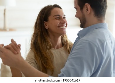 Happy millennial multiethnic man and woman dance waltz together at home, show love and affection in relationship. Smiling young couple lovers celebrate wedding marriage anniversary. Bonding concept.