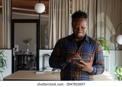 Happy millennial self employed professional using tablet in office. Young African American hipster guy, student, employee using virtual app, online service on pad computer, chatting, browsing