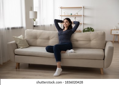 Happy millennial Vietnamese girl sit relax on sofa in living room look in window distance dreaming thinking. Smiling young asian woman renter rest on couch at home visualize imagine on weekend. - Shutterstock ID 1836020428