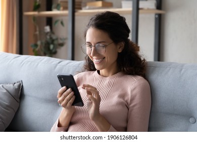 Happy millennial woman relaxing on comfortable sofa, enjoying web surfing information in internet or using mobile software application, communicating distantly with friends in social networks at home. - Shutterstock ID 1906126804