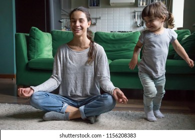 Happy Mindful Single Mother Doing Morning Exercises In Yoga Pose With Kid Daughter Playing At Home, Smiling Young Mom Having Fun Practicing Meditation Relaxing On Stress Free Weekend With Child Girl