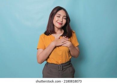 Happy mindful thankful young woman holding hands on chest smiling isolated on blue background feeling no stress, gratitude, mental health balance, peace of mind concept. - Shutterstock ID 2180818073