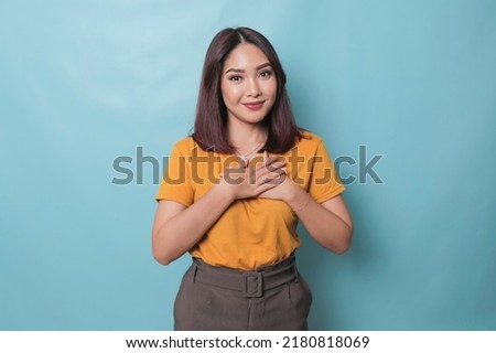 Happy mindful thankful young woman holding hands on chest smiling isolated on blue background feeling no stress, gratitude, mental health balance, peace of mind concept.