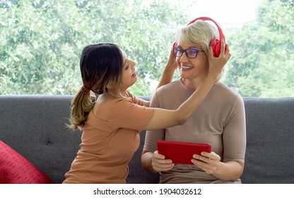 Happy mix skin family living together, asian daughter help her adopted caucasian mother listen to music with headphones through a tablet computer. - Powered by Shutterstock