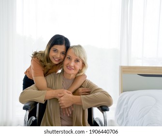 Happy Mix Skin Family Living Together, Adopted Asian Daughter  Cuddle Caucasian Mother Sitting On A Wheelchair With Smiles. Concept Of Love And Sharing Time Of Family, Mother Or Daughter In Law.