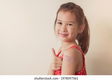 Happy Mixed Asian Girl  Giving Thumb Up And Showing Her Arm With Bandage After Got Vaccinated Or Inoculation, Child Immunization, Covid Delta Vaccine