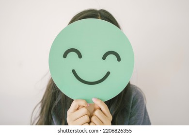 Happy mixed Asian girl holding smile emoji face, positive mental health concept