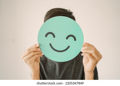 Happy mixed Asian teen boy holding smile emoji face, positive mental health concept