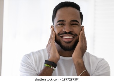 Happy mixed race African man touching soft stubble, stylish beard, smiling at camera. Metrosexual guy satisfied with aftershave balm, moisturizing cream. Male beauty care concept. Head shot portrait