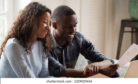 Happy Mixed Race Couple Consider Domestic Financial Bills, Pay Online On Computer, Smiling African American Husband And Wife Read Bank Documents Check Bank Account On Laptop, Glad To Get Refund