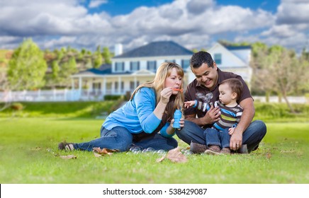 Happy Mixed Race Ethnic Family Playing with Bubbles In Their Front Yard.