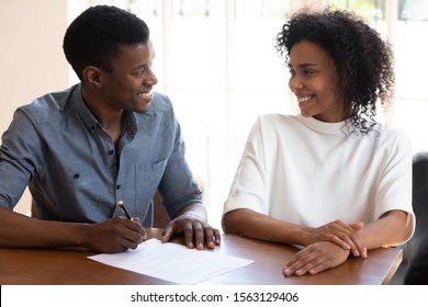 Happy Mixed Race Family Couple Discussing Insurance Contract Details Before Signing At Office. Smiling African American Clients Negotiating Terms Of Conditions Before Putting Signature On Agreement.