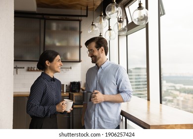 Happy Mixed Race Family Couple Drink Tea Coffee At New Modern Apartment Flat By Picture Window. Loving Young Spouses Indian Wife Caucasian Husband Enjoy Talking Holding Cups With Hot Drinks At Kitchen