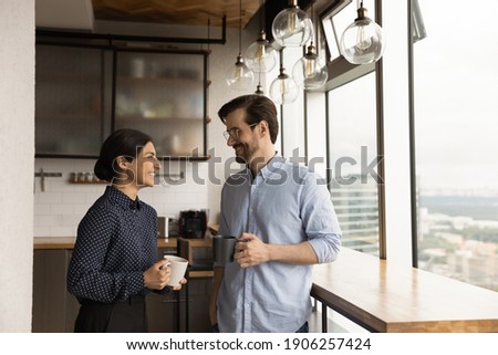 Happy mixed race family couple drink tea coffee at new modern apartment flat by picture window. Loving young spouses indian wife caucasian husband enjoy talking holding cups with hot drinks at kitchen Foto stock © 