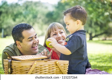 Happy Mixed Race Family Enjoy A Picnic At The Park.