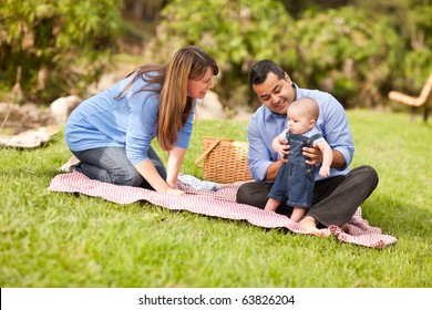 Happy Mixed Race Family Having A Picnic And Playing In The Park.