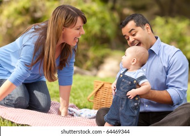 Happy Mixed Race Family Having A Picnic And Playing In The Park.