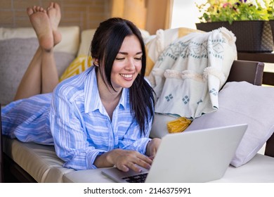 Happy Mixed Race Freelancer Woman Eating Fresh Seasonal Strawberry Lying On Comfy Couch At Outdoor Summer Terrace. Smiling Female Enjoying Appetizing Berries Having Break Working Remotely On Laptop Pc