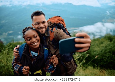 Happy mixed race hiking couple taking selfie from the top of the mountain. - Powered by Shutterstock