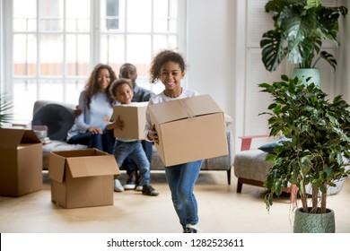 Happy Mixed Race Kids Running Carrying Boxes On Moving Day, Black Family Tenants Relocation Concept, African American Parents And Children Laughing Playing In New Home Flat Having Fun In Living Room