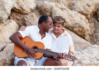 Happy Mixed Race, Middle Age Couple Embracing While Walking On The Beach Holding A Guitar. Man Holding Guitar With Woman.