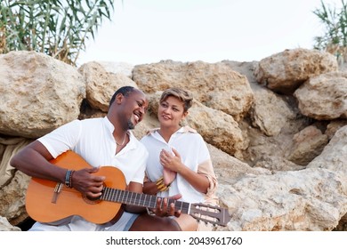 Happy mixed race, middle age couple embracing while walking on the beach holding a guitar. Man holding guitar with woman.