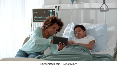 Happy mixed race mother and son using digital tablet in ward at hospital. African woman visiting son in clinic and showing photos on tablet pc. - Powered by Shutterstock