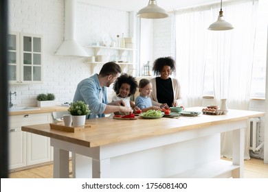 Happy mixed race multinational family with daughters prepare vegetable organic fresh salad, enjoy pastime cooking process in cozy kitchen, healthy eating, parents teach kids, weekend at home activity - Shutterstock ID 1756081400