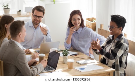 Happy Mixed Race Office Workers At Business Meeting Having Fun. Diverse Men And Women Laughing Sitting At Desk, Share Ideas. Smiling Black Female Speaker Talking. Team Work, Team Building Concept