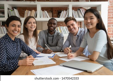 Happy mixed race students gathered in classroom, looking at camera. Smiling group of diverse young people holding video call lecture with abroad online course professor, ready to write down notes. - Shutterstock ID 1470542333