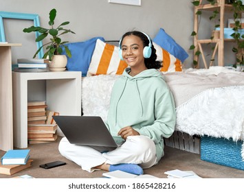 Happy Mixed Race Teen School Girl Distant College Student Wearing Headphones Virtual Remote E Learning Using Laptop In Bedroom Looking At Camera. Distance Education Classes, Studying Online At Home.