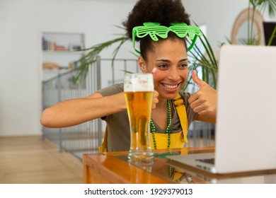 Happy mixed race woman with beer celebrating st patrick's day making video call giving thumbs up. staying at home in isolation during quarantine lockdown. - Powered by Shutterstock