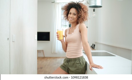 Happy mixed race woman holding orange juice and looking to camera. - Powered by Shutterstock