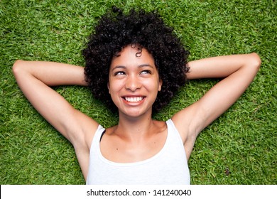 Happy mixed race woman lying down on green grass with hands behind her head.