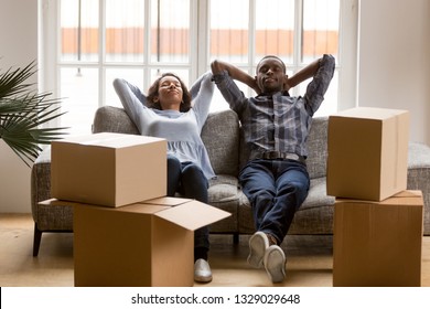 Happy Mixed Race Young Husband And Wife Relax On Couch At Home Tired On Moving Day, Peaceful Black Couple Man And Woman Lying In Living Room With Cardboard Boxed Around, Exhausted Relocating