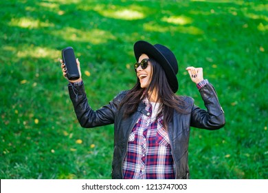 Happy Mixed Race Young Woman Listening To Music With Wireless Portable Speaker. Hispanic Hipster Girl Dancing To Rhythm And Singing Along Melody In The Park