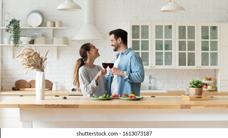 Happy mixed race young woman cheering glasses of red wine with smiling man, enjoying romantic family time in modern kitchen. Excited married couple spending free weekend time together at home. - Powered by Shutterstock