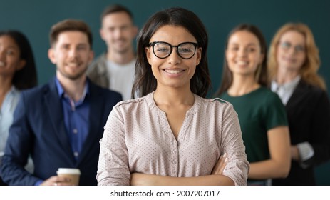 Happy mixed raced Black female business leader, confident business woman standing in front of team, smiling at camera. Office employee posing with coworkers in background. Head shot portrait