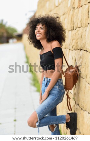 Fröhliche gemischte Frau mit Afrohaar, die im Freien steht.